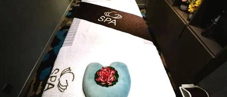 A spa area with a massage table, a heart-shaped cushion, and a black towel with 'SPA' written on it.
