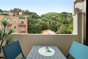 A balcony with a table and chairs, overlooking a hillside with buildings and trees.