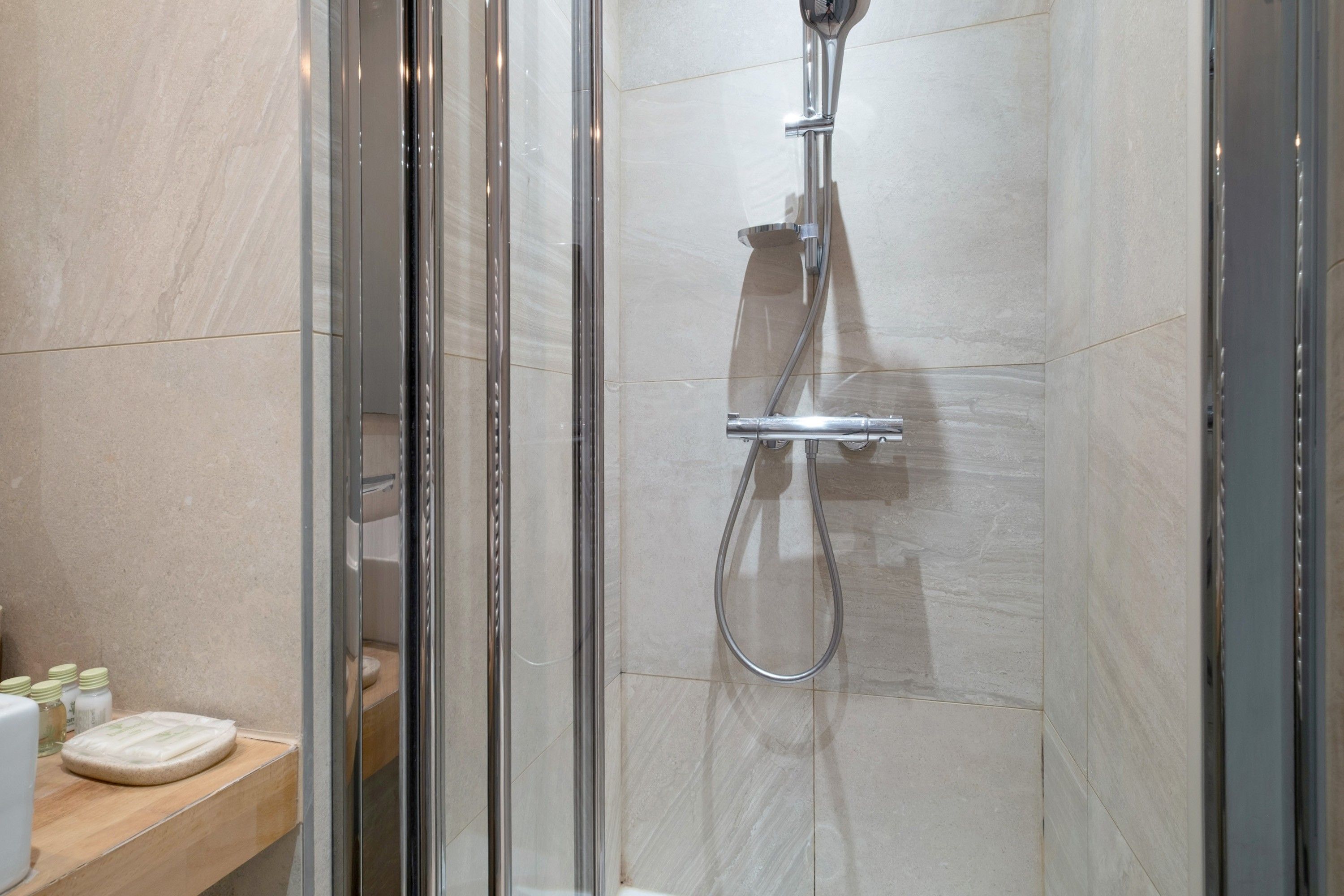 Een douche met glazen wand, een handdouche en een wandmengkraan.
