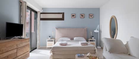 A bedroom with a bed, a television, a sofa, and a window with curtains.