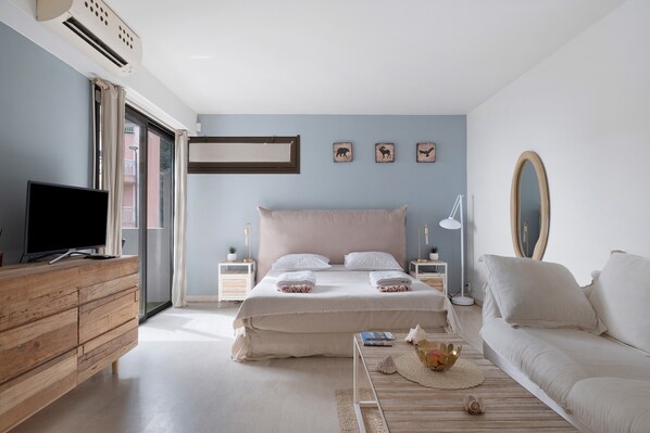 A bedroom with a bed, a television, a sofa, and a window with curtains.