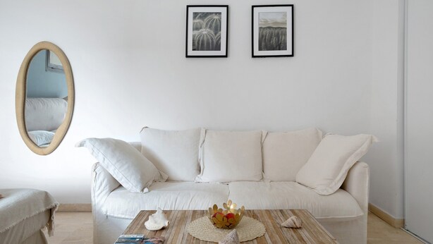 En minimalistisk stue med en hvid sofa, et rundt spejl og to billeder i rammer på væggen.