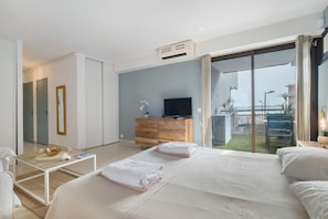 Una habitación de hotel moderna con una cama grande, televisión, cómoda de madera y vista al mar.