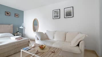 Un salon minimaliste avec un canapé blanc, une table basse et une petite table d’appoint sur laquelle se trouve une lampe. Deux tableaux encadrés sont accrochés au mur.
