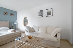 Una sala de estar minimalista con un sofá blanco, una mesa de centro y una mesita auxiliar con una lámpara. Hay dos cuadros en la pared.