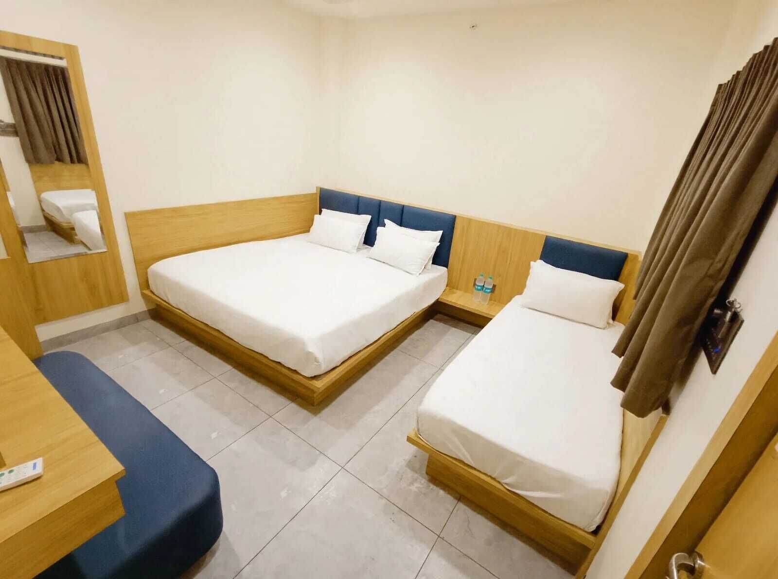 A hotel room with two beds, a desk, and a mirror.