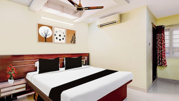 Habitación de hotel con cama, mesita de noche, un jarrón de flores y un ventilador de techo.