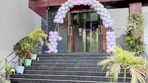 Entrada de hotel con puerta de vidrio, escalinata de mármol y un arco decorativo de globos.