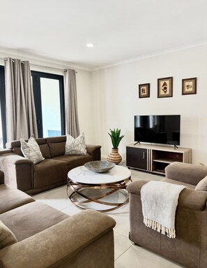 Ein modernes Wohnzimmer mit einer Sofagarnitur, einem Couchtisch, einem Fernseher und gerahmten Bildern an der Wand.
