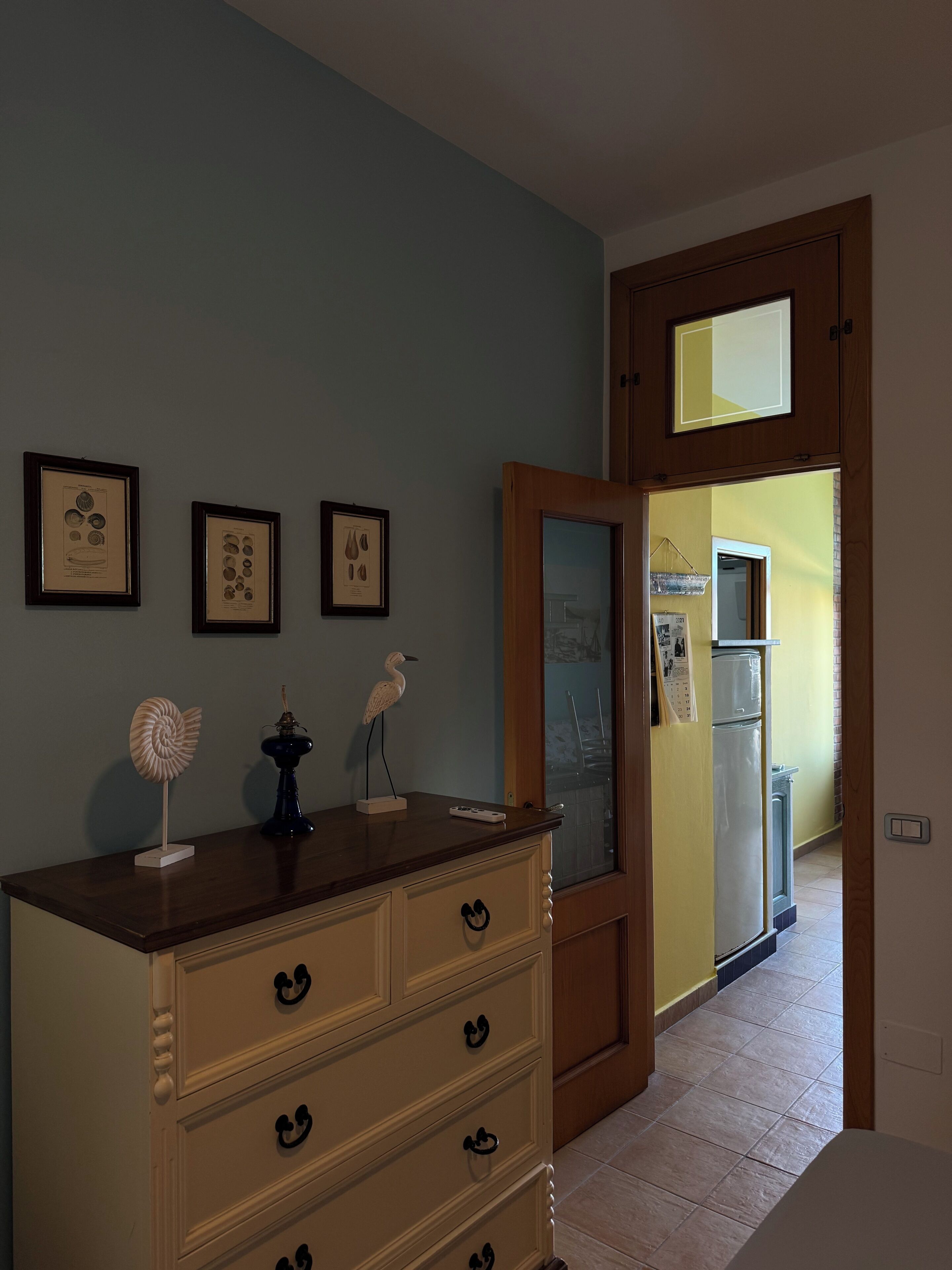 A room with a wooden dresser, a mirror, and framed botanical prints on the wall.