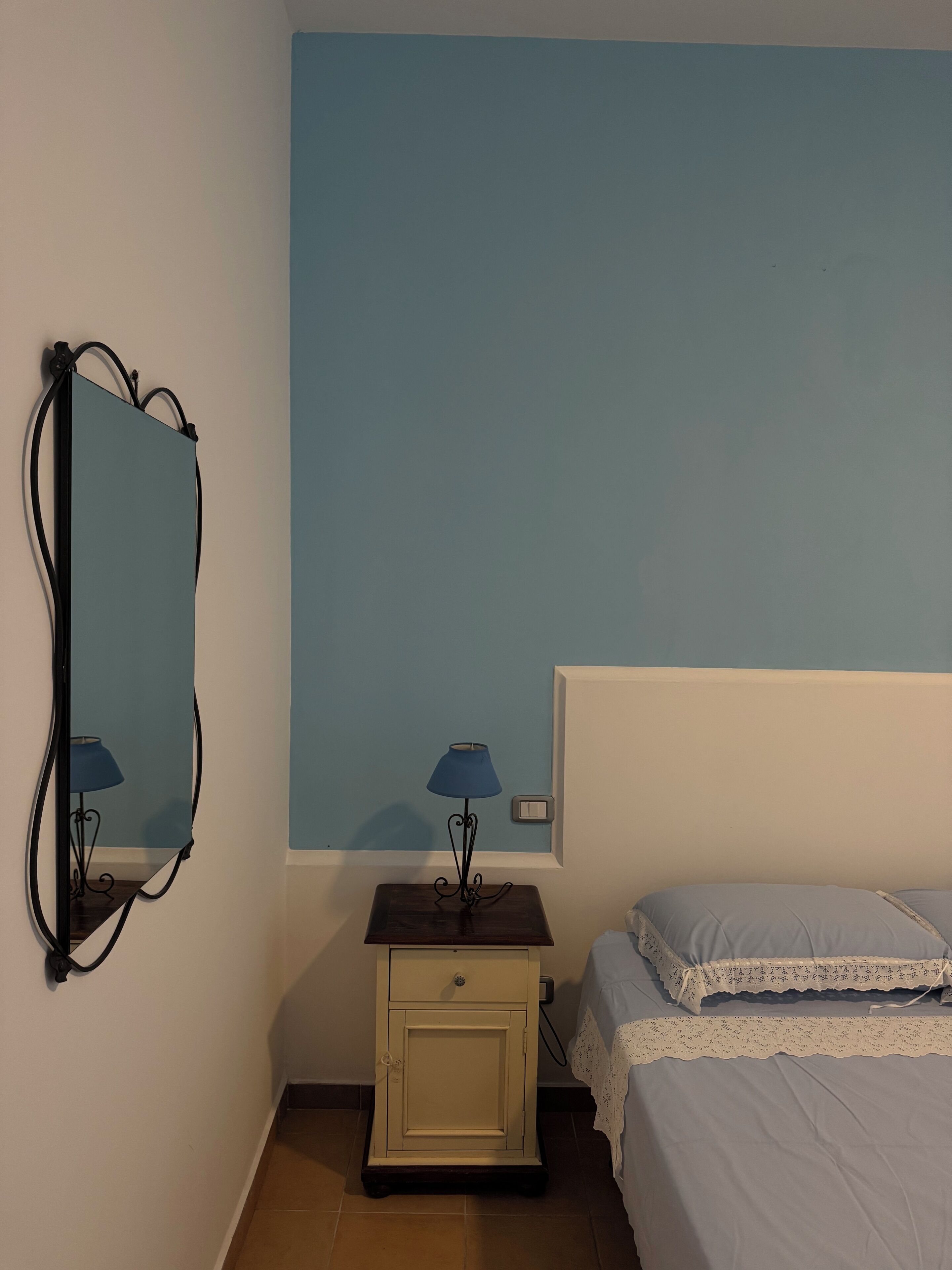 Un dormitorio con cama, mesita de noche con lámpara, cómoda y espejo en la pared.