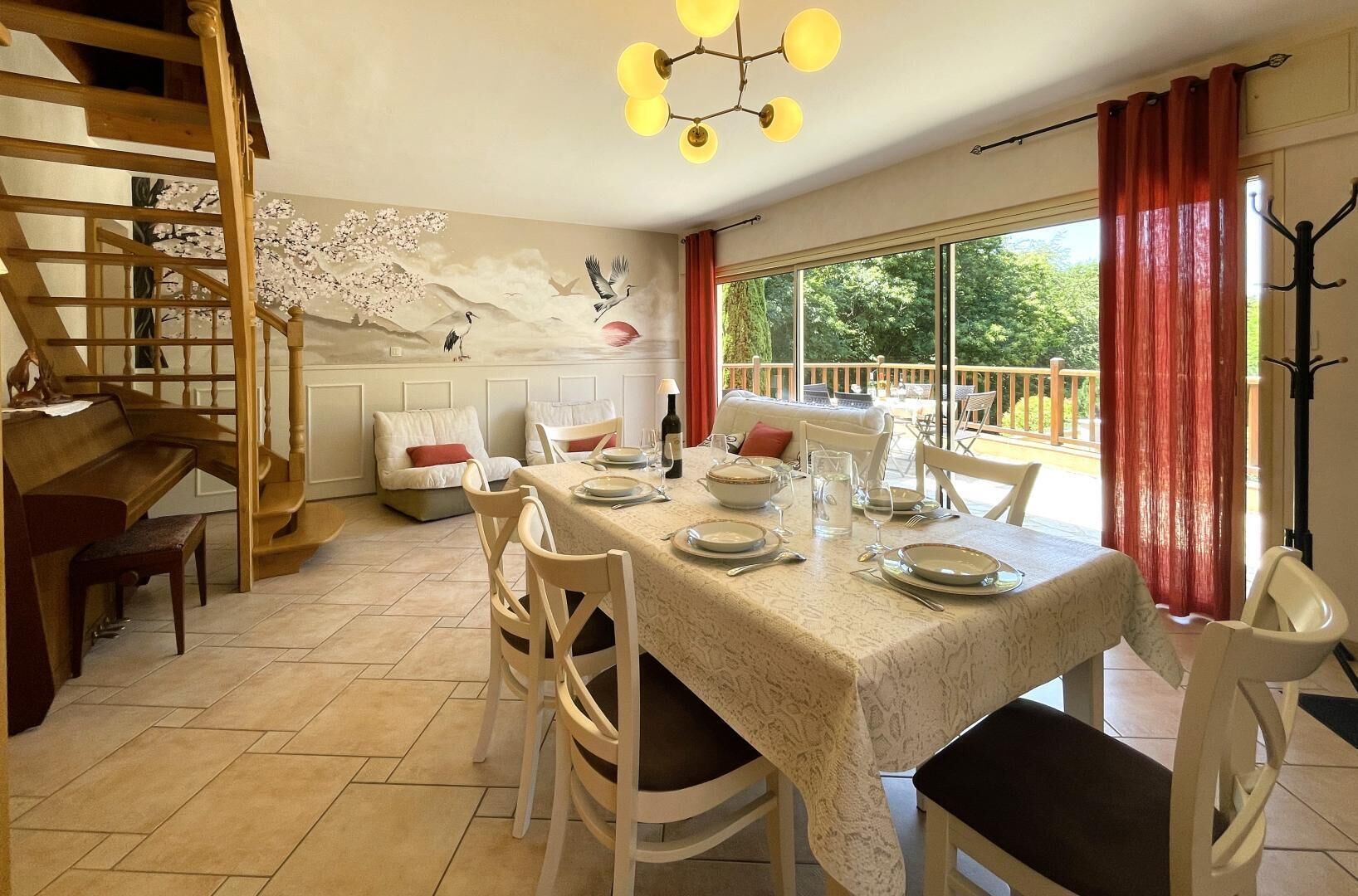 Un comedor con una mesa dispuesta para cuatro personas, una escalera y vistas al exterior.