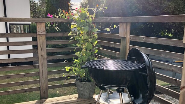 A wooden deck with a barbecue grill, a potted plant, and a wooden fence. - GG Village (Askim)