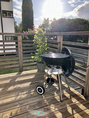 A wooden deck with a barbecue grill, a potted plant, and a wooden fence.
