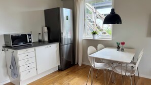 A compact kitchen with a microwave, refrigerator, and a dining table with chairs. - GG Village (Askim)
