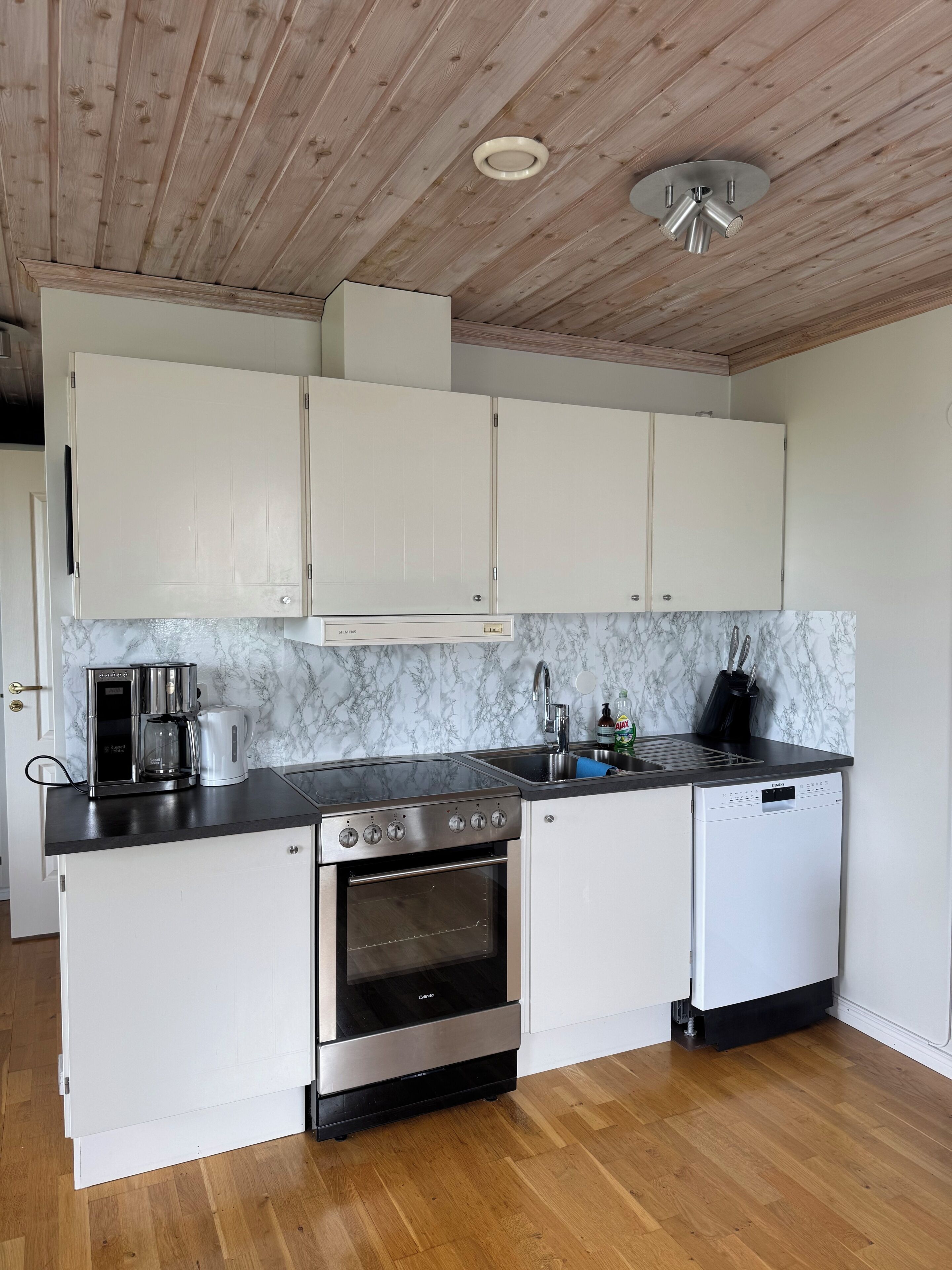 A kitchen with white cabinets, a stainless steel stove, a dishwasher, and a marble backsplash.