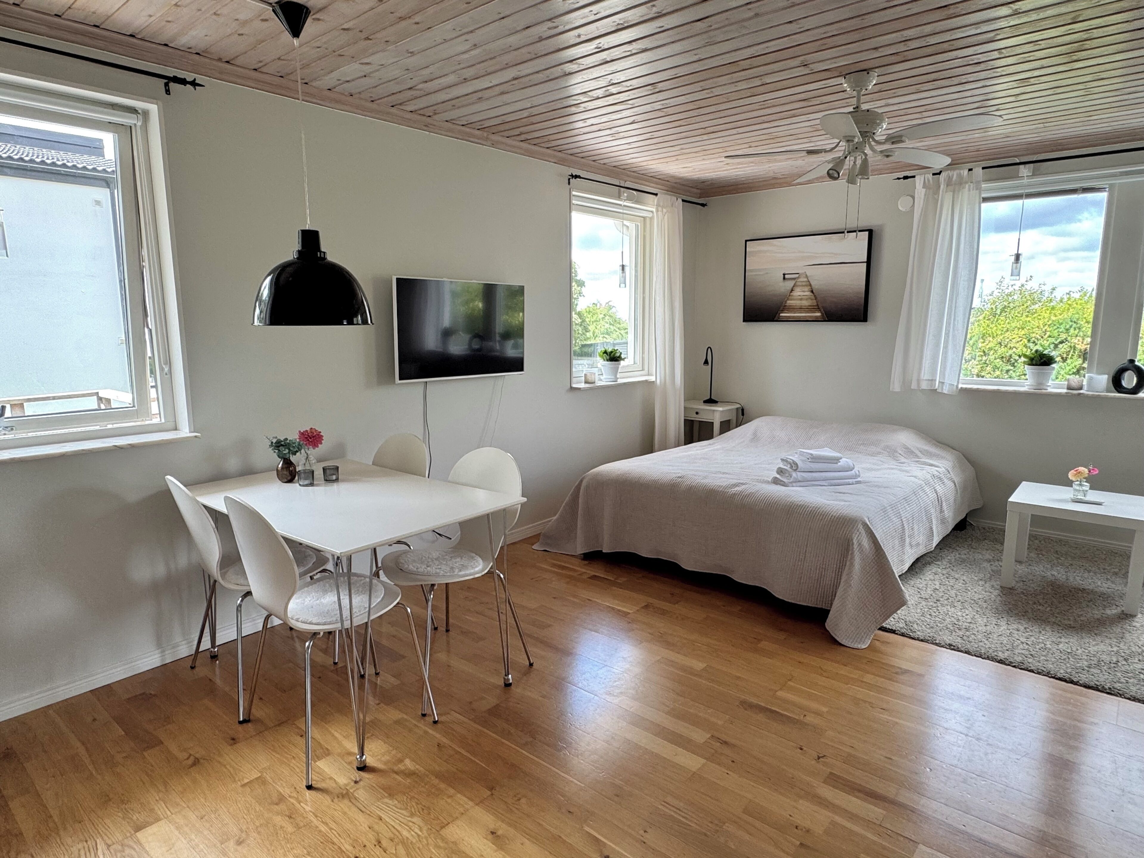 Ett modernt sovrum med en säng, ett skrivbord, stolar, en tv och en takfläkt.