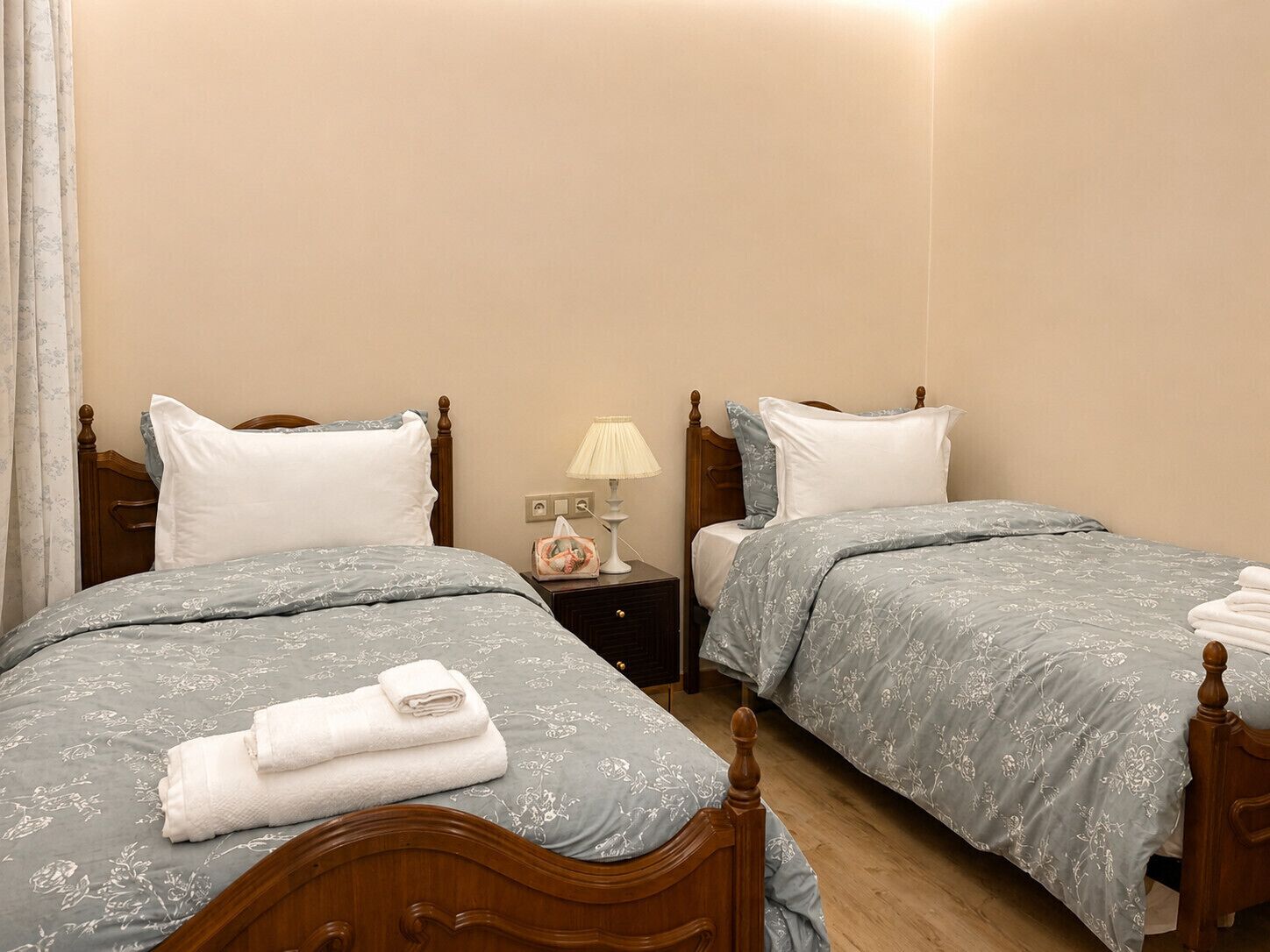 Une chambre d’hôtel avec deux lits, chacun doté d’une tête de lit en bois, d’une table de chevet avec une lampe et d’une fenêtre avec des rideaux.