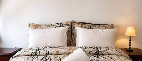 A neatly made bed with a floral-patterned duvet, two pillows, and a rolled white towel.
