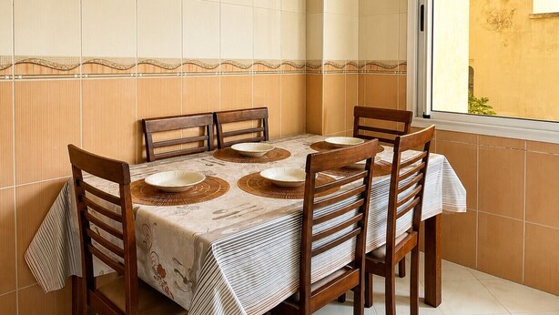A dining area with a table set for four, wooden chairs, and a window with a view of the outside. - Kortobi Central Stay – 2-Bedroom Apartment Near the Old Medina (Tanger)