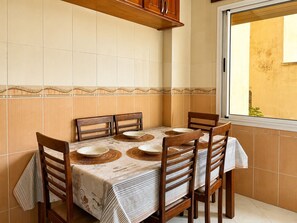 A dining area with a table set for four, wooden chairs, and a window with a view of the outside. - Kortobi Central Stay – 2-Bedroom Apartment Near the Old Medina (Tanger)