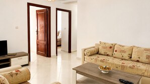 A living room with a sofa, a coffee table, and a television. There are two doors leading to other rooms. - Kortobi Central Stay – 2-Bedroom Apartment Near the Old Medina (Tanger)