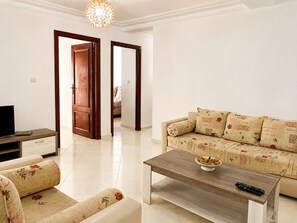 Ein Wohnzimmer mit einer Couch, einem Couchtisch und einem Fernseher. Zwei Türen führen in andere Räume.