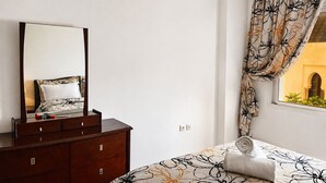 A bedroom with a bed, a dresser, a mirror, and a window with curtains. - Kortobi Central Stay – 2-Bedroom Apartment Near the Old Medina (Tanger)