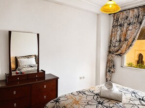 Ein Schlafzimmer mit einem Bett, einem Schminktisch, einem Spiegel und einem Fenster mit Vorhängen.