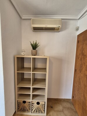 Ein Eckzimmer mit einer Holzhockerreie, einem kleinen Topfpflanzen und einer Wandklimaanlage sowie einer Holztür.