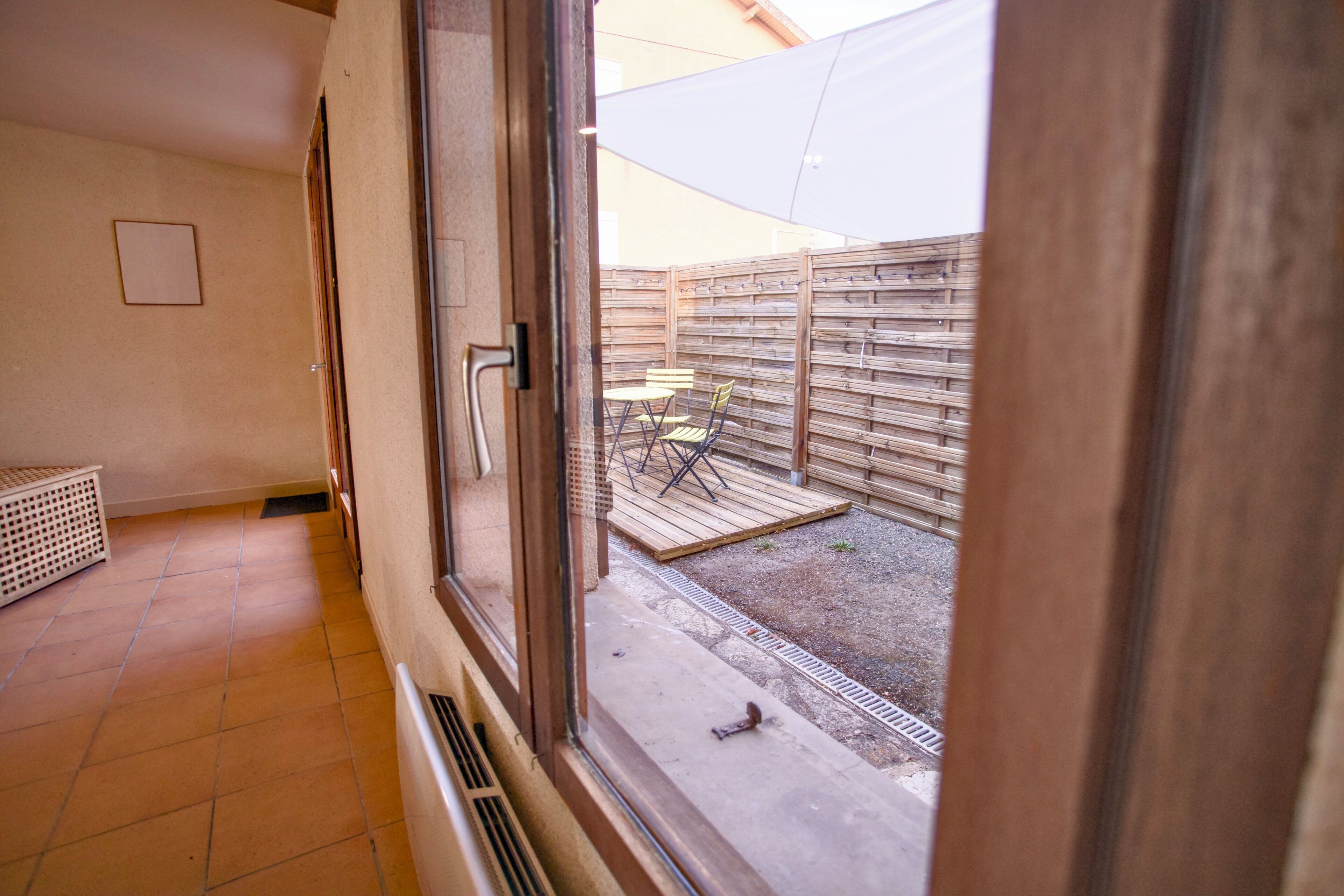 A room with a large window, a door, and a view of an outdoor patio area with a wooden fence and outdoor furniture.