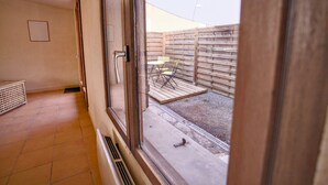 A room with a large window, a door, and a view of an outdoor patio area with a wooden fence and outdoor furniture. - Quiet cottage with a terrace, 3 minutes from Albi (Castelnau-de-Lévis)