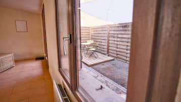 A room with a large window, a door, and a view of an outdoor patio area with a wooden fence and outdoor furniture.