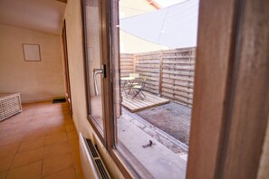 A room with a large window, a door, and a view of an outdoor patio area with a wooden fence and outdoor furniture. - Quiet cottage with a terrace, 3 minutes from Albi (Castelnau-de-Lévis)