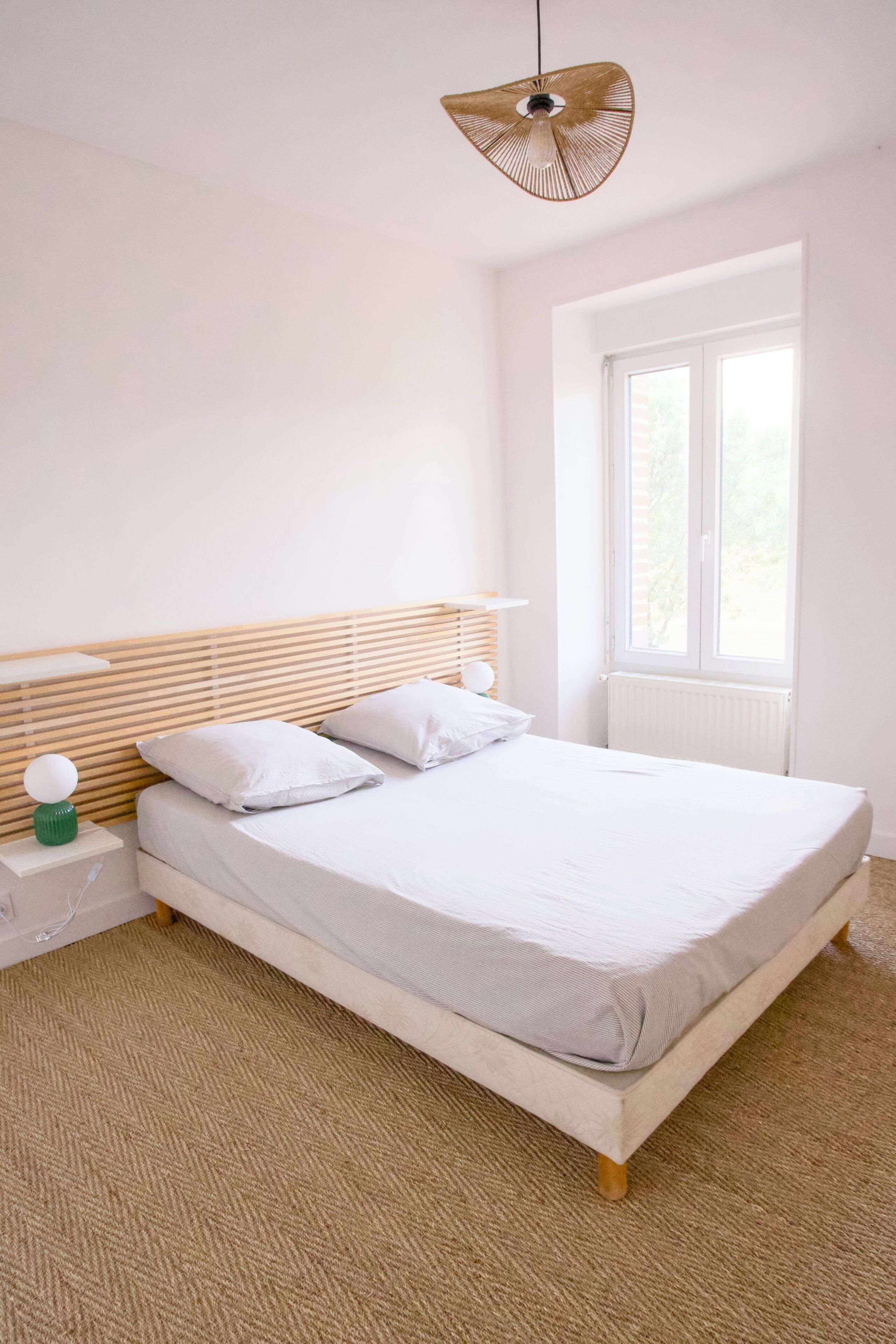 Une chambre à coucher avec un lit, une table de chevet, une lampe et une fenêtre.