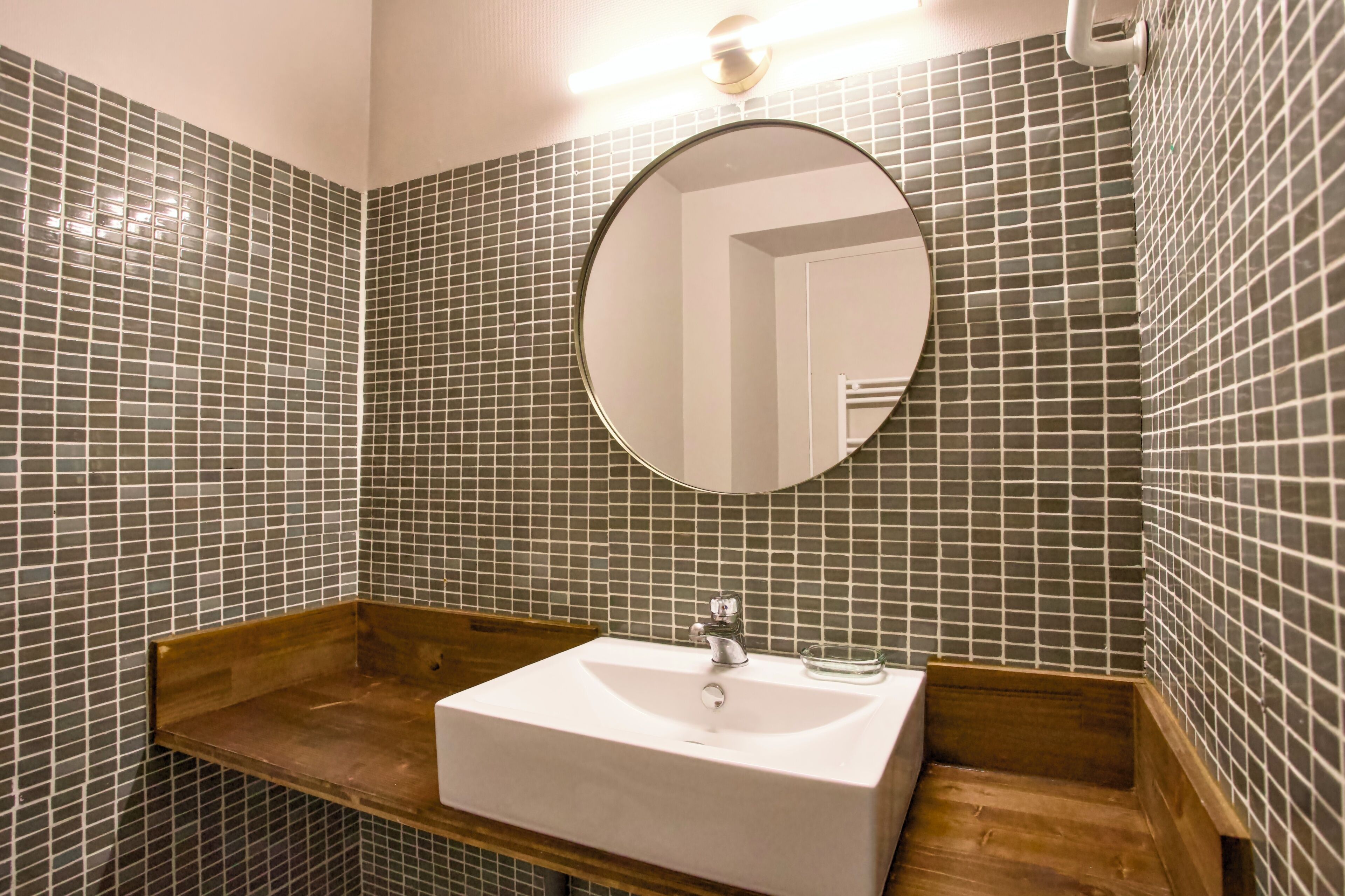 Een badkamer met een wit wastafelmeubel, een ronde spiegel en betegelde wanden.