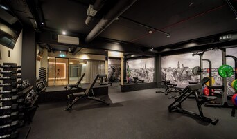 A gym with weightlifting equipment, treadmills, and a cityscape mural.