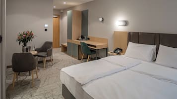 A hotel room with a large bed, a desk, a chair, and a small table with a vase of flowers.