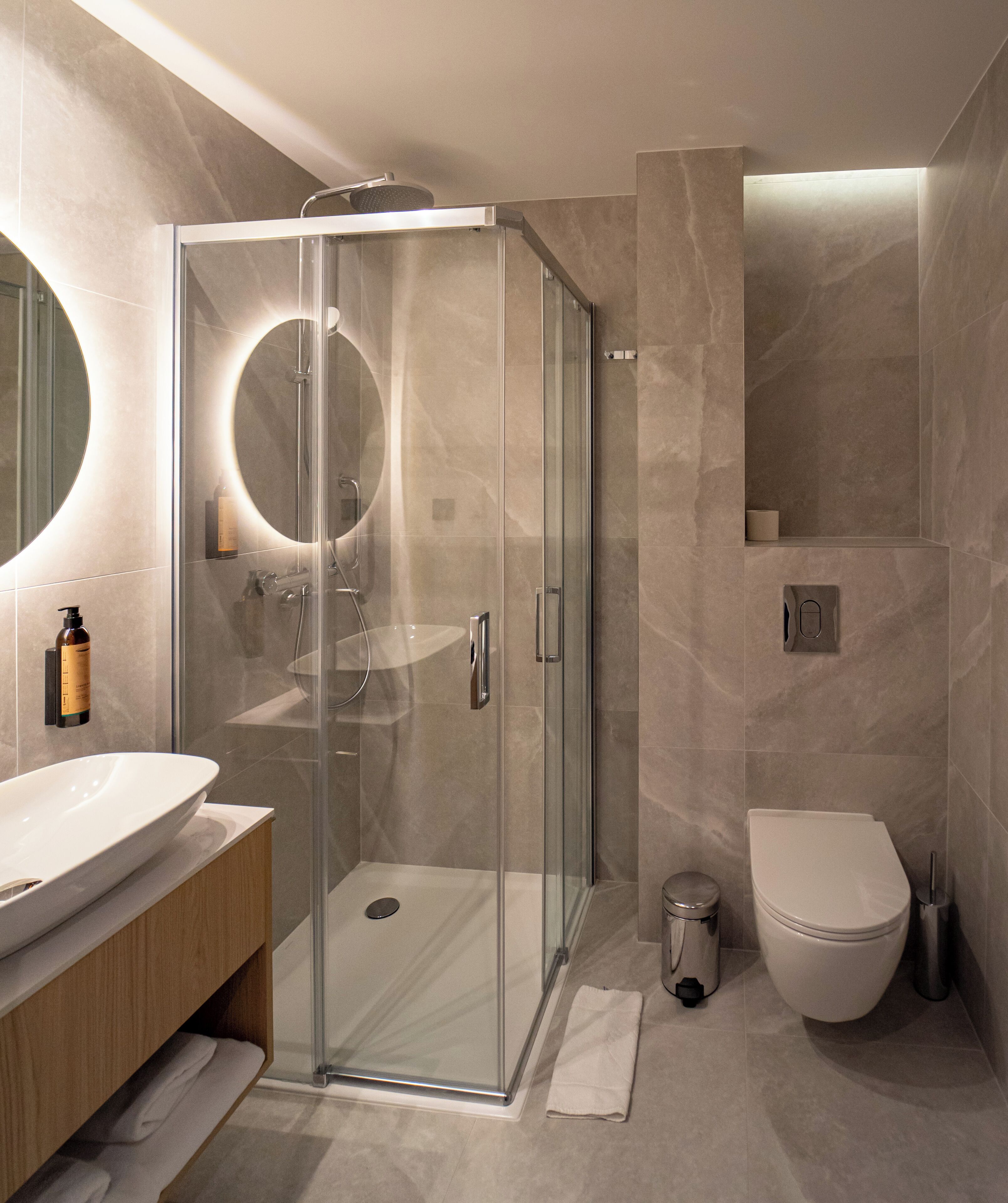 Un baño moderno con ducha de vidrio, un espejo redondo y un inodoro.