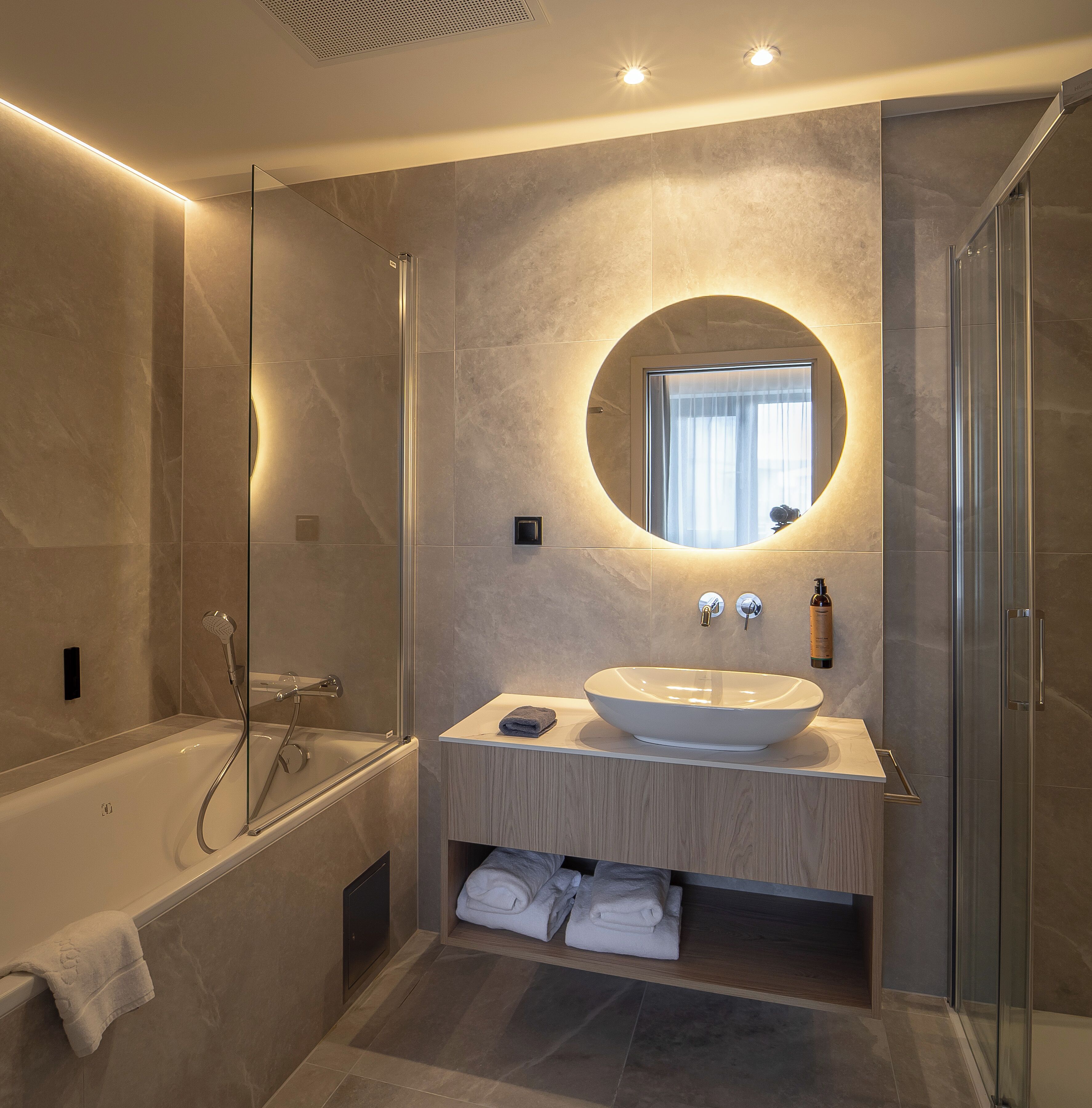Un baño moderno con una bañera independiente, un espejo redondo y un lavabo empotrado con tocador.