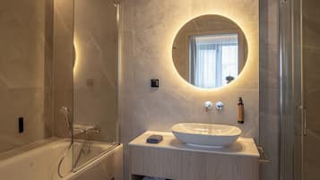 Un baño moderno con una bañera independiente, un espejo redondo y un lavabo empotrado con tocador.