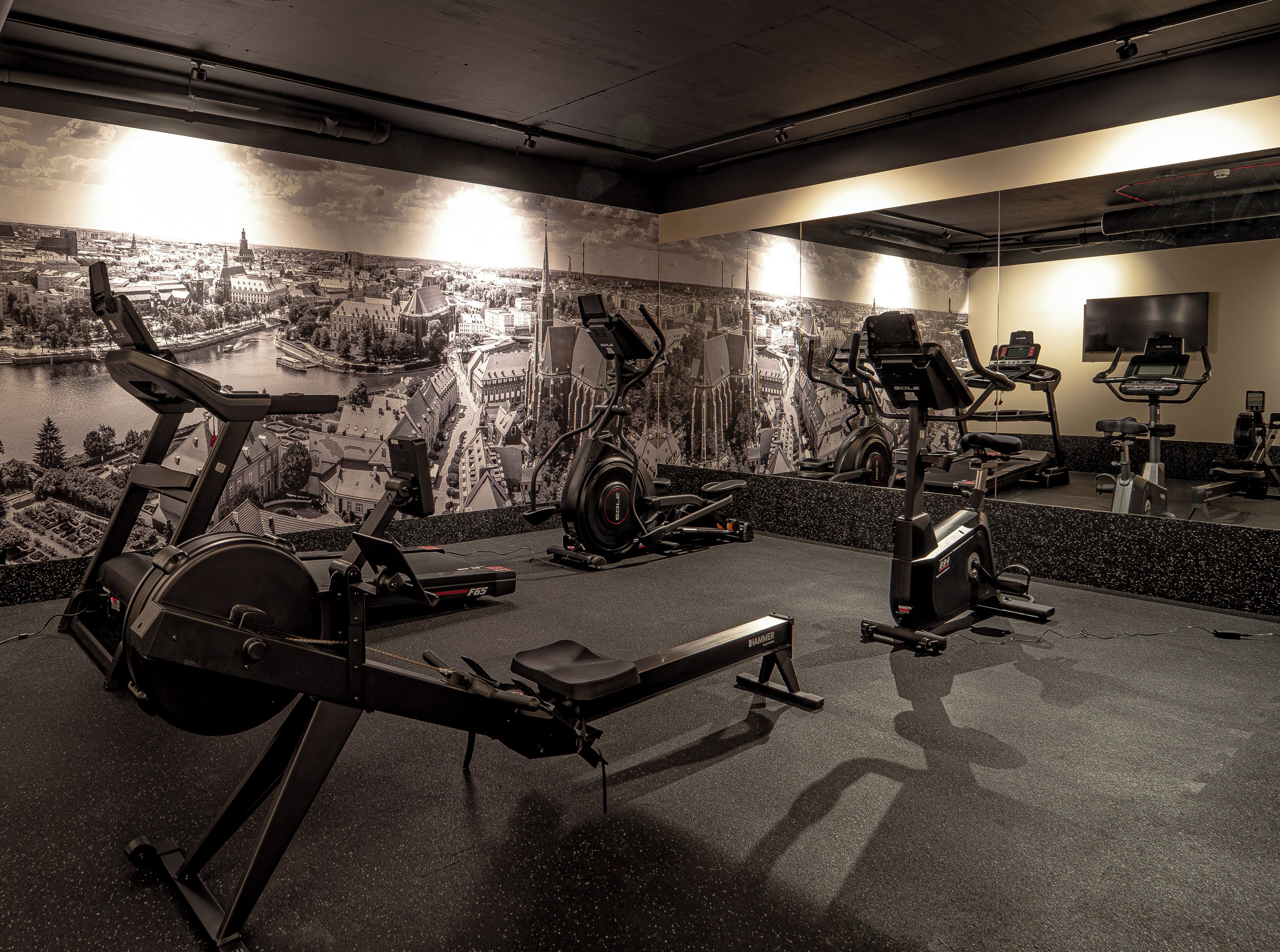 Un gimnasio con bicicletas estáticas, cintas de correr y un espejo que refleja los equipos.