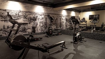 Un gimnasio con bicicletas estáticas, cintas de correr y un espejo que refleja los equipos.