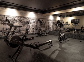 Un gimnasio con bicicletas estáticas, cintas de correr y un espejo que refleja los equipos.