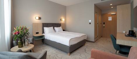 A hotel room with a bed, bedside tables, a desk, a chair, and a small table with a vase of flowers.