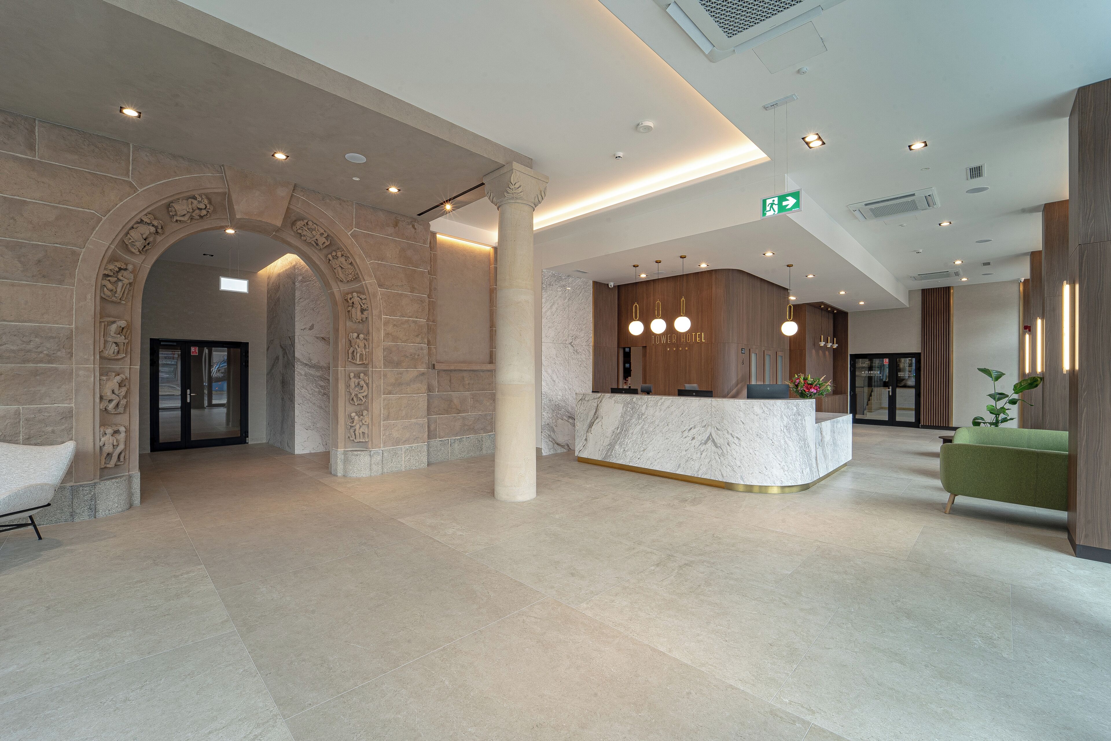 Un hall d’hôtel avec un comptoir de réception en marbre, un canapé vert et une arche en pierre.