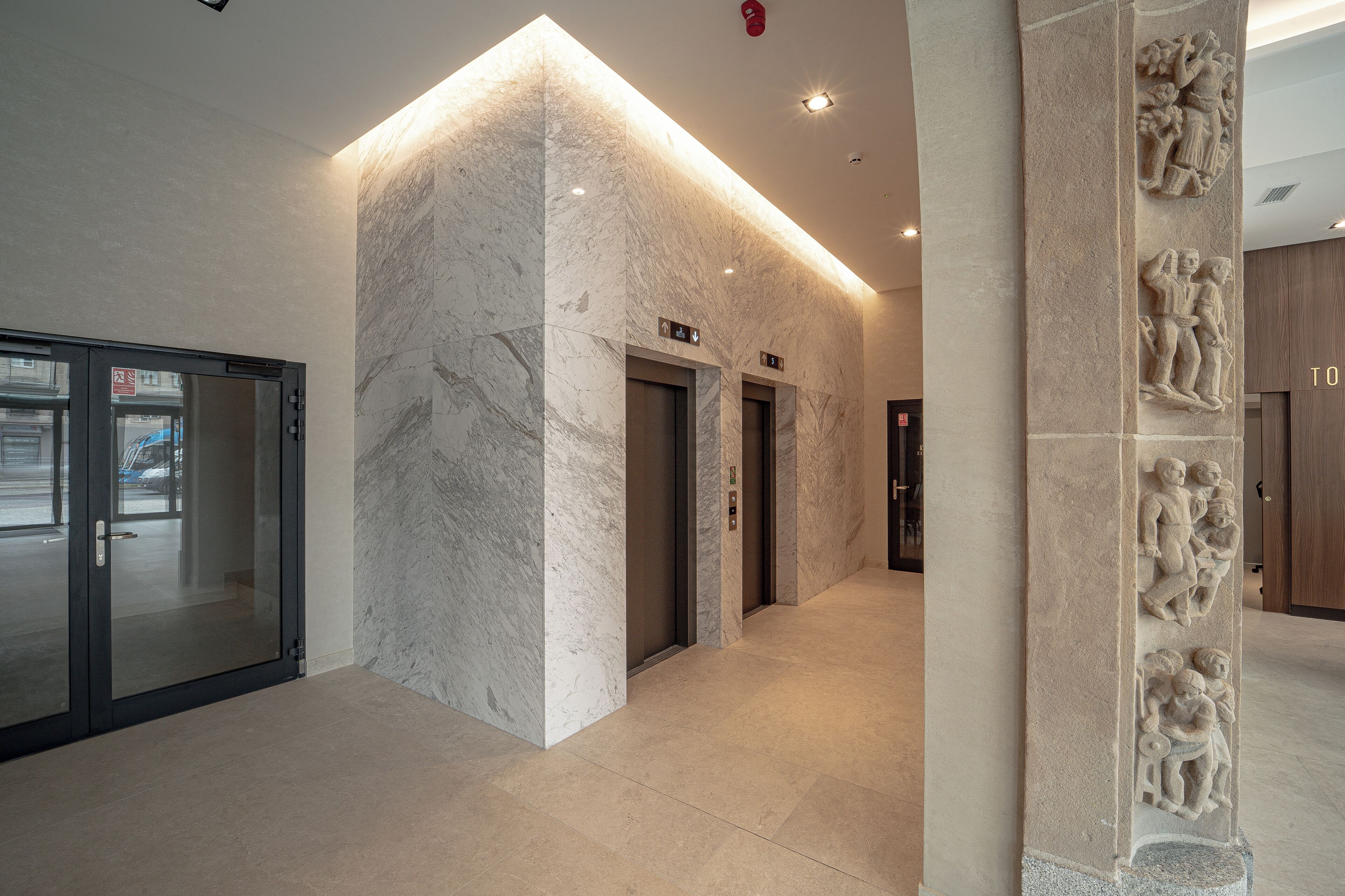 Un interior moderno con paredes de mármol, puerta de entrada de vidrio y un pasillo que conduce a los ascensores.