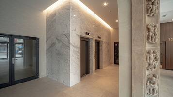 Un interior moderno con paredes de mármol, puerta de entrada de vidrio y un pasillo que conduce a los ascensores.