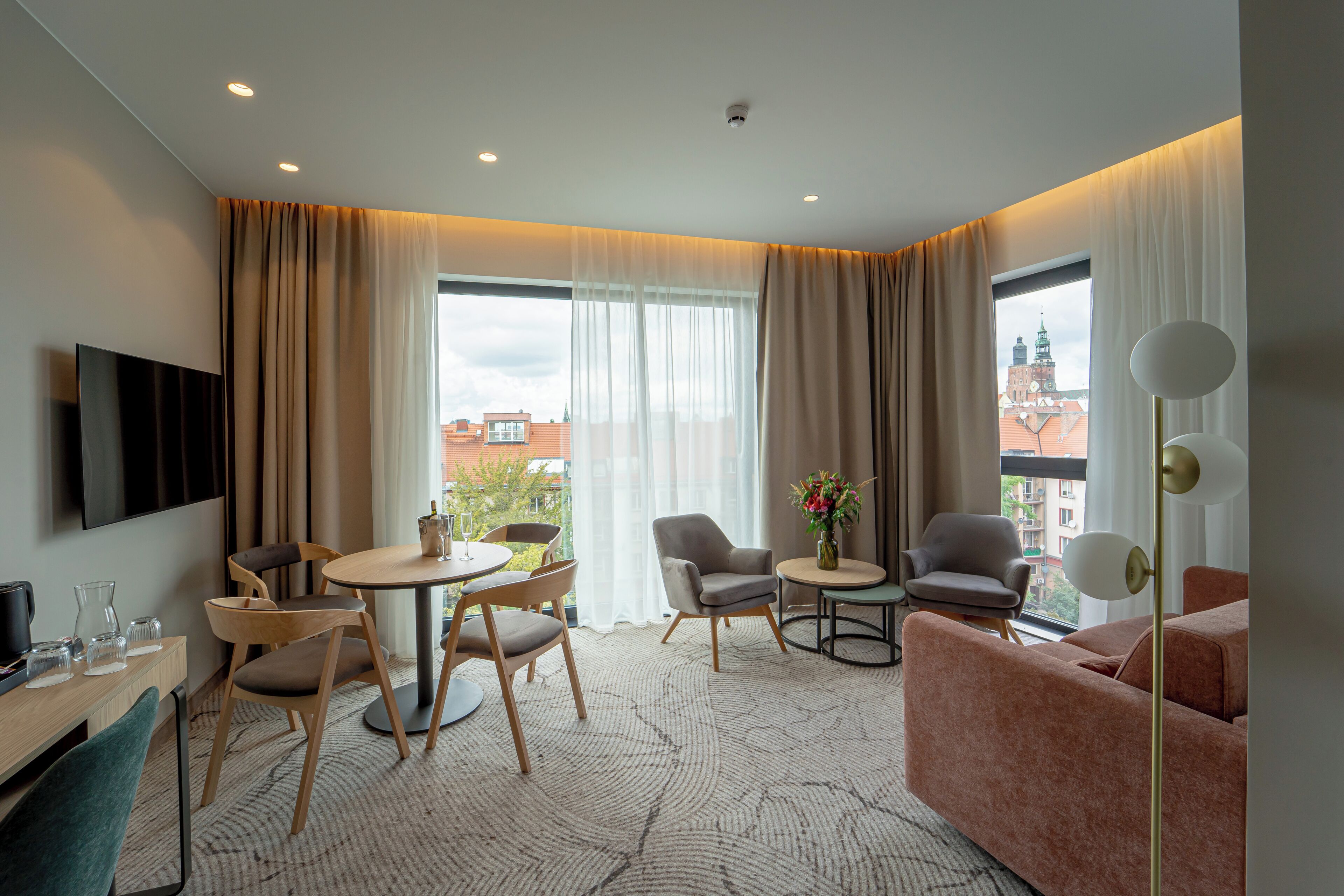 Habitación de hotel moderna con zona de comedor, sofá, televisor y vistas a la ciudad.