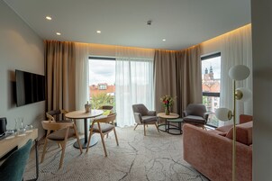 Habitación de hotel moderna con zona de comedor, sofá, televisor y vistas a la ciudad.